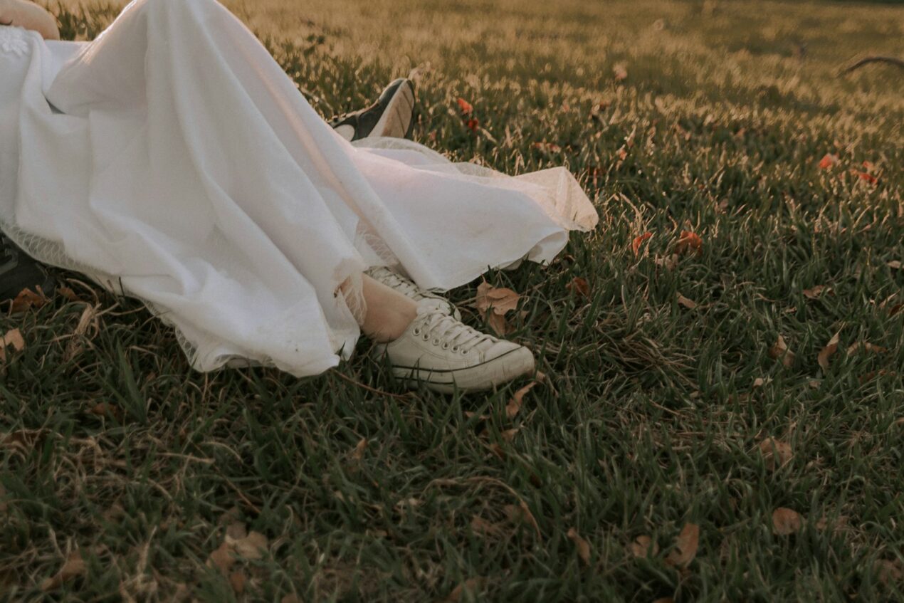 Bride in a wedding gown lying in the grass, wearing flat white canvas sneakers instead of heels.