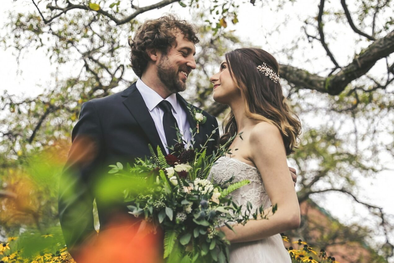 Bride in a lace wedding dress and groom standing under autumn trees at an outdoor fall wedding venue